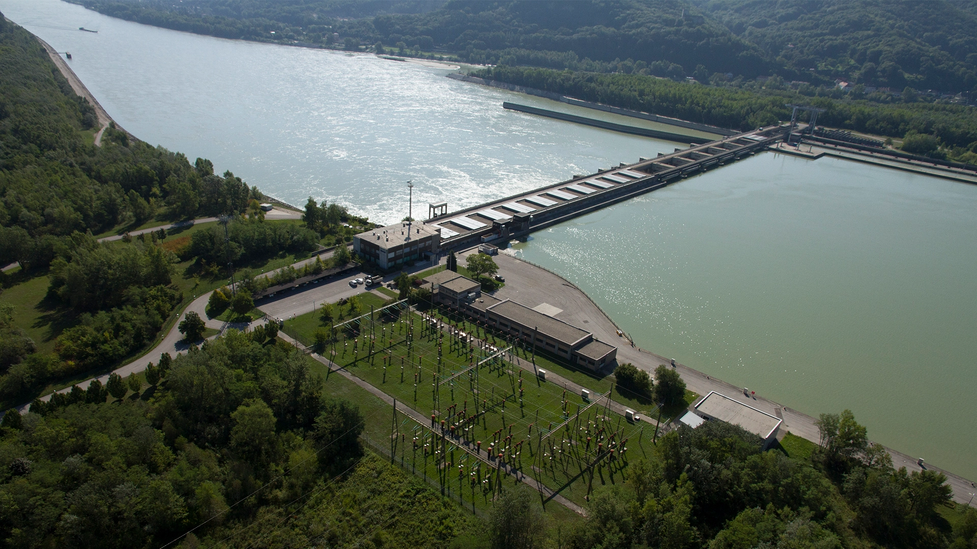 Aus der Vogelperspektive ist das Laufkraftwerk Greifenstein abgebildet. In der Mitte fließt die Donau. Zu sehen sind die Staumauer und Stromleitungen auf der rechten Uferseite.