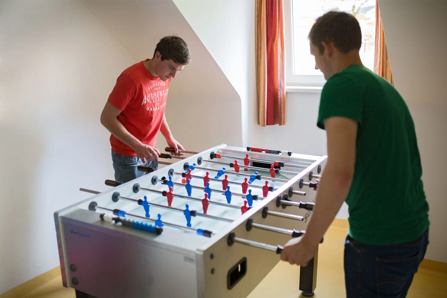 Zwei VERBUND-Lehrlinge in Zivilkleidung spielen gegeneinander am Tischfussball.
