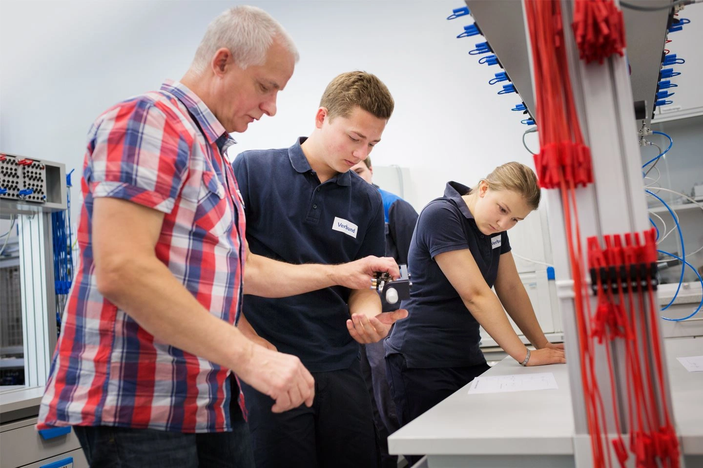 Ein Ausbilder bei VERBUND erklärt zwei Auszubildenden eine neue Aufgabe. Die Lehrlinge trägen dunkelblaue Shirts und blicken auf ein Blatt Papier.