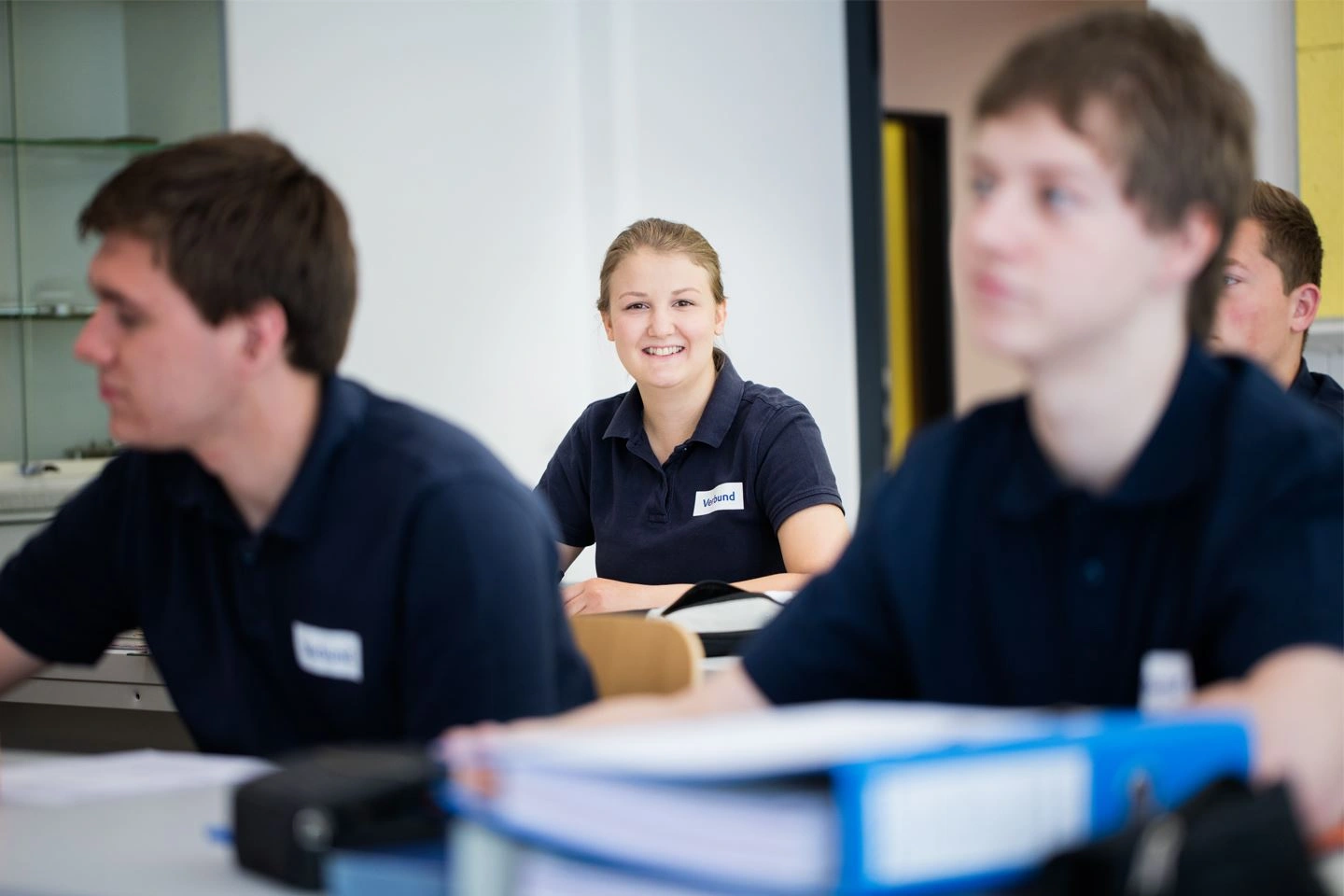 Wir sehen VERBUND-Lehrlinge im Klassenraum Eine Auszubildende blickt lächelnd in die Kamera.