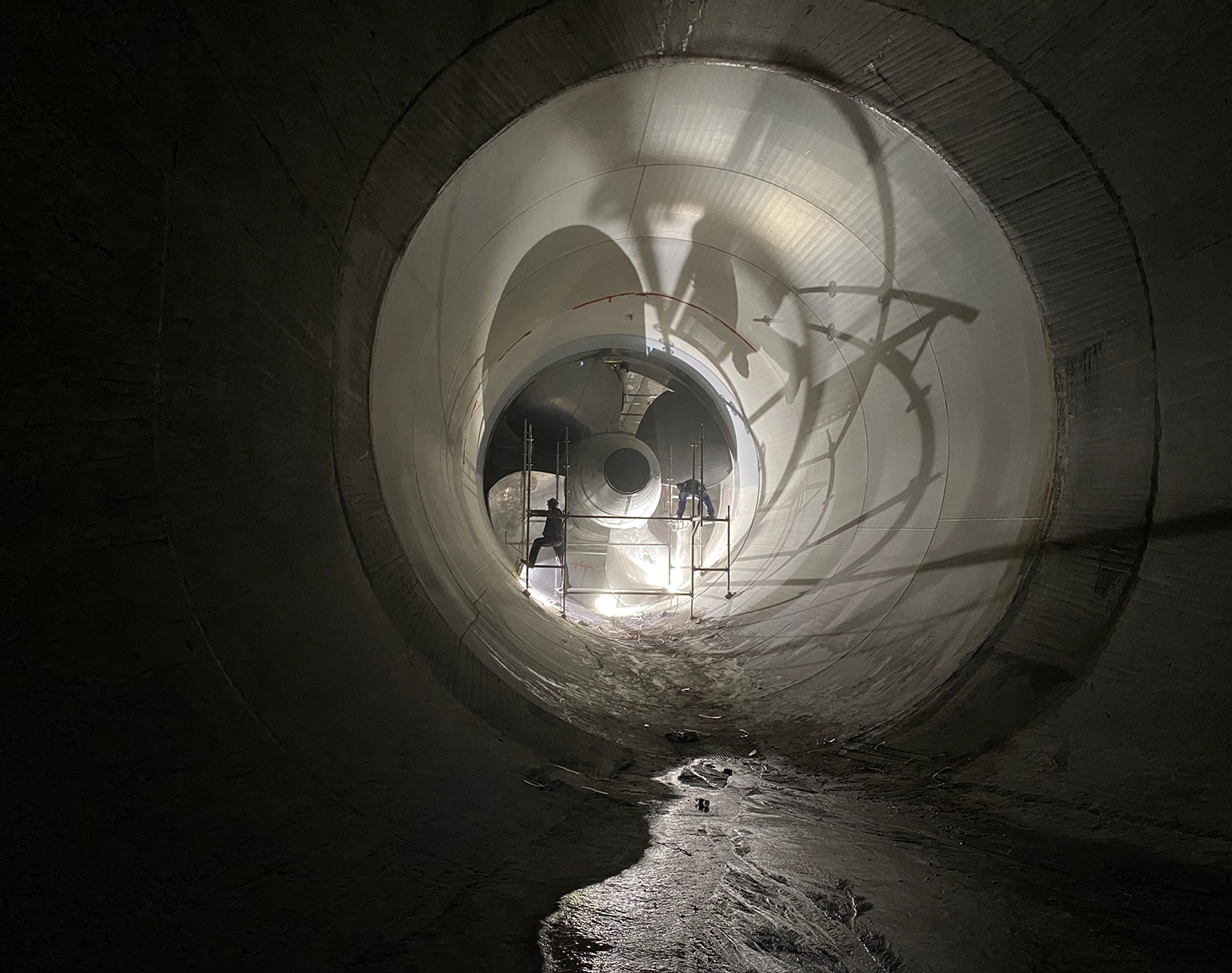 Das Bild zeigt die Turbine des Laufkraftwerk Altenwörth während der Revision. Das gesamte Bild ist dunkel und Mitarbeiter:innen arbeiten an der Turbine.