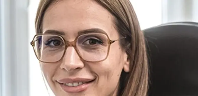 The VERBUND employee has long blonde hair. She is wearing glasses, a white T-shirt and a black blazer.